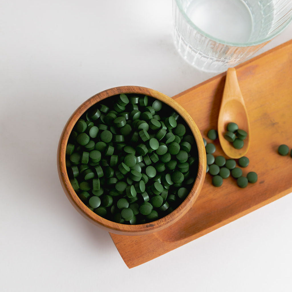 Wooden bowl with green tablets on a white surface next to a glass of water.
