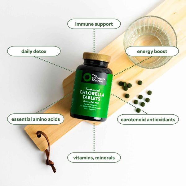 Bottle of fermented Chlorella tablets with health benefits listed on a wooden board