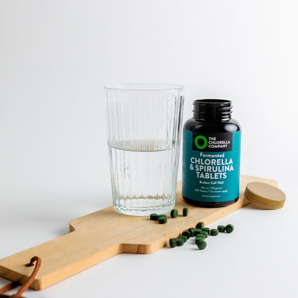 Fermented Chlorella & Spirulina tablets bottle with a glass of water on a wooden board