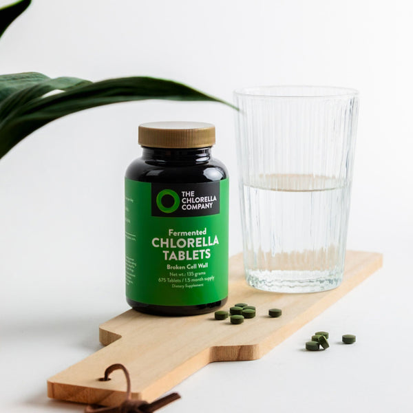 Fermented Chlorella tablets bottle with a glass of water on a wooden board